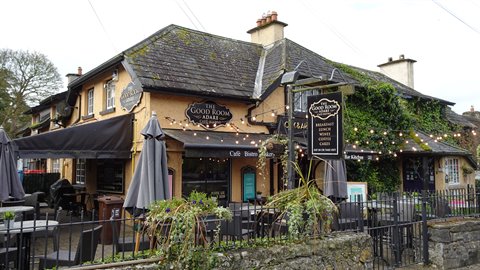 Old stone pub with black signs, umbrellas and string lights under overcast sky
