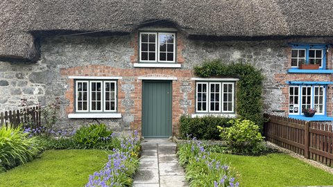 Rural stone cottage with thatched roof, blue window frames and flowering garden