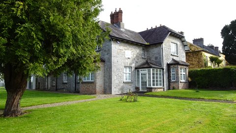 Grey stone house with bay windows, green lawn and tree, soft daylight