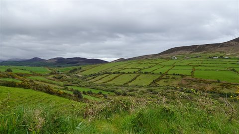 Green fields divided by stone walls under a cloudy sky among hills