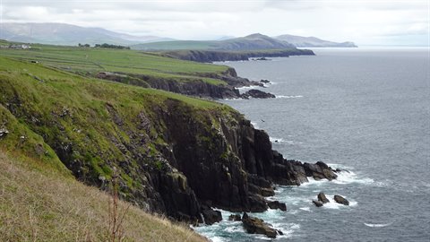 Grassy cliffs over the ocean under cloudy sky, rocky coastline in diffused light