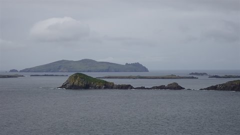 Green rocky islands on grey sea under cloudy sky, soft light