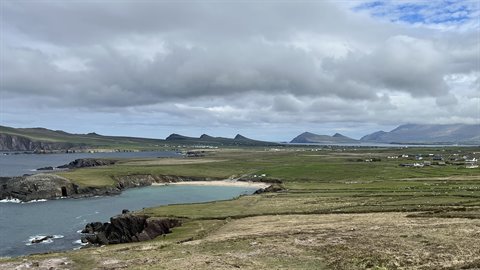 Sandy cove between green cliffs, distant mountains, cloudy sky, diffused light
