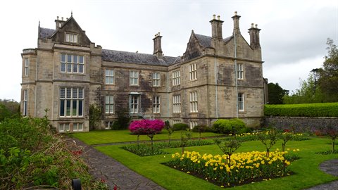 Old stone mansion with flower gardens of yellow tulips under cloudy sky