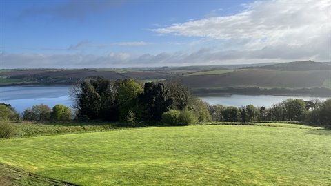 Green meadow before a wide estuary under partly cloudy sky, morning light