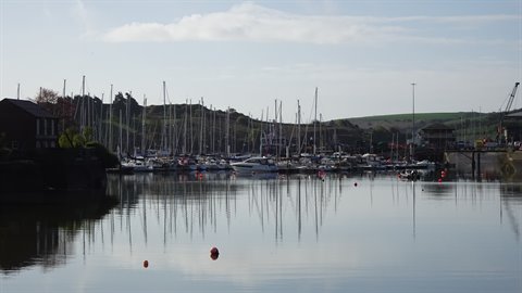 Sailboats moored in marina, masts reflected in calm water under cloudy sky