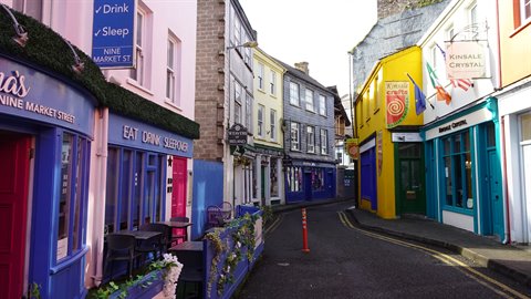 Narrow street lined with colorful shopfronts and pubs under soft daylight