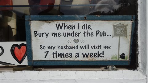 Painted wooden sign with humorous phrase hanging in a pub window