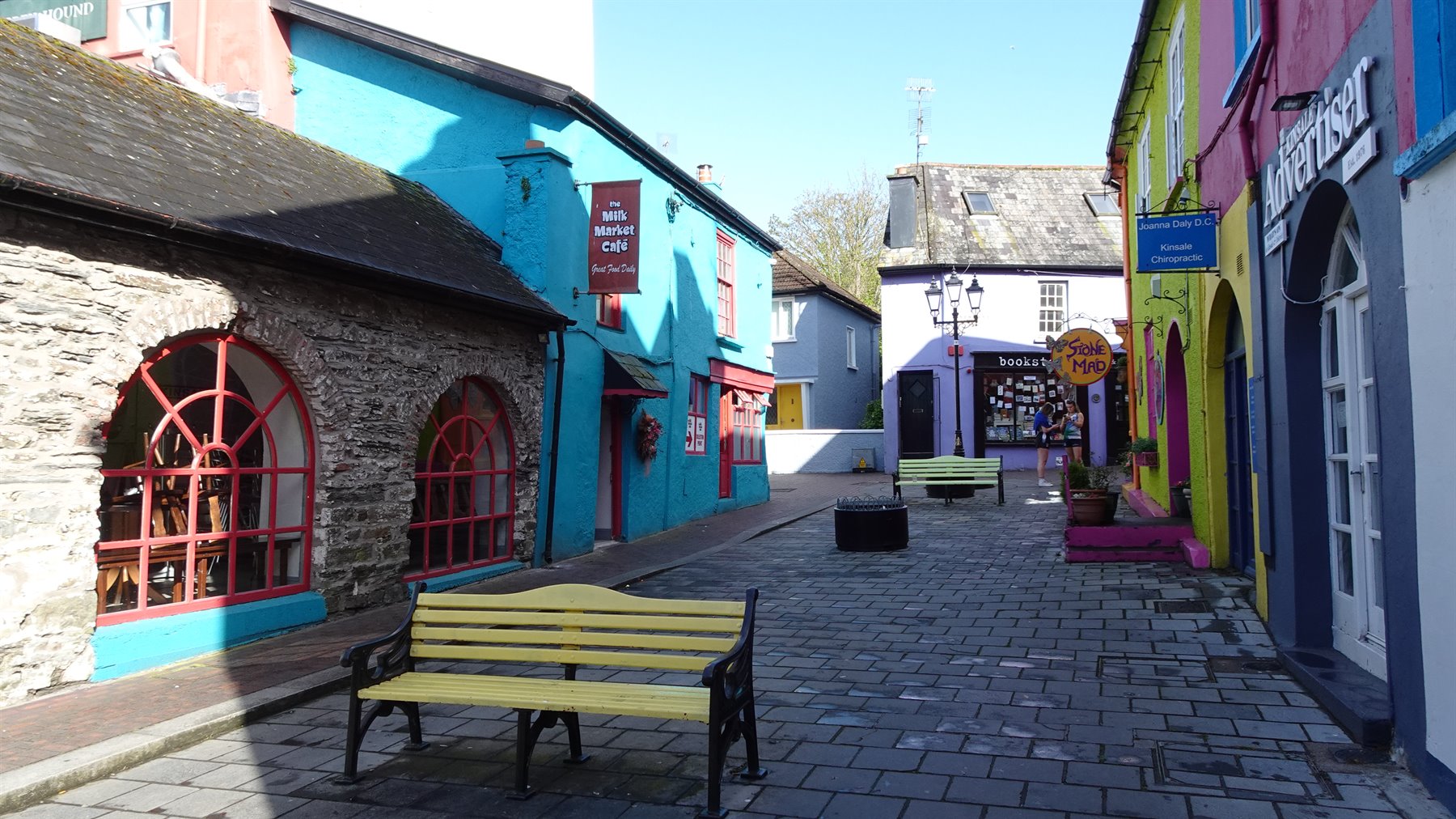 Yellow bench on cobbled street between colorful buildings, sunny light, no people