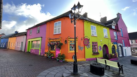 Colorful shop facades on cobbled square, black lamppost and green bench
