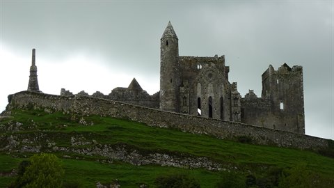 Stone castle ruins on a grassy hill under a cloudy sky