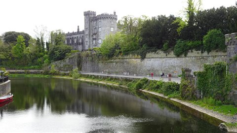 Medieval stone castle above a calm river, green trees, soft light