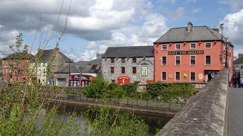 River below a stone bridge with colorful houses and pubs under a cloudy sky
