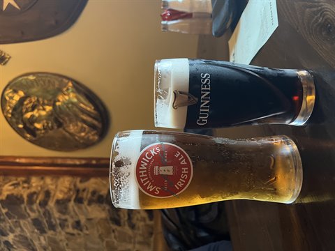 Guinness and Smithwick's beer glasses on wooden pub table, warm light