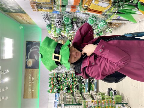 Woman in green leprechaun hat among souvenirs and plush toys in shop