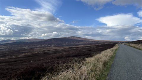 Asphalt road through moorland and rolling hills, cloudy sky, daylight