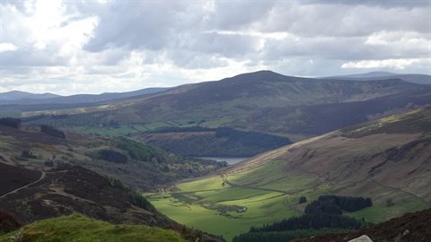 Green hills and a lake among mountains under cloudy sky