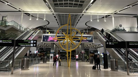 Golden spiral sculpture inside an airport terminal, escalators and travelers under artificial lights
