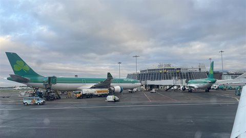 Green and white airplanes parked at terminal, service vehicles, cloudy sky, soft light