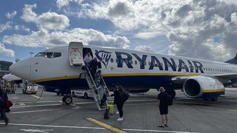 Passengers boarding a Ryanair plane via stairs, cloudy sky, tarmac