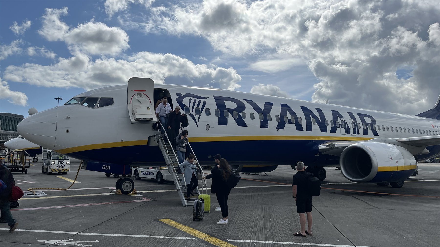 Passengers boarding a Ryanair plane via stairs, cloudy sky, tarmac