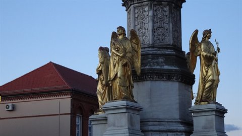 Golden angel statues around a carved stone column at dusk