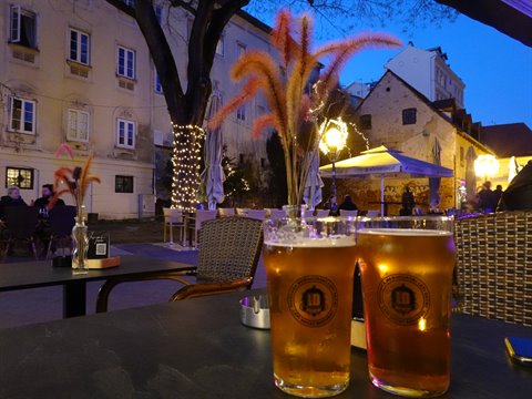 Two beer glasses on outdoor table among illuminated historic buildings