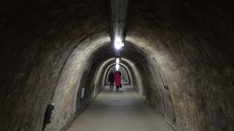 Tunnel carved in rock, ceiling lights, woman in red coat walking