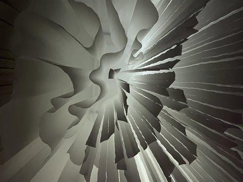 Abstract sculpture of folded white paper, light radiating from the center