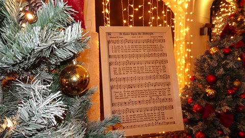 Christmas carol sheet music board among decorated trees with golden baubles and warm lights