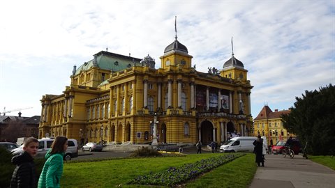 Tourists walk past the yellow Croatian National Theatre in Zagreb with domes