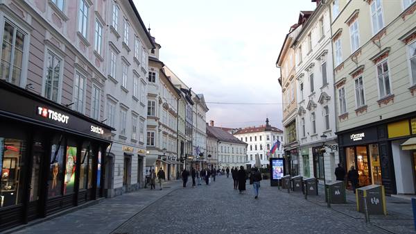 Cobbled pedestrian street in Ljubljana with pastel buildings and people under grey light