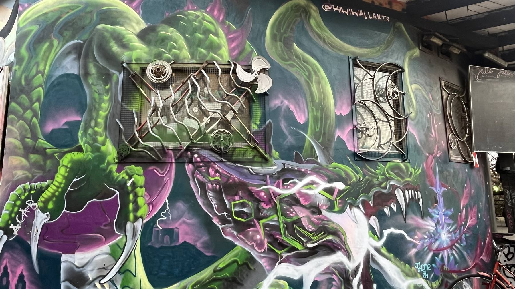 Murale di draghi verdi e viola con graffiti, luce diurna su muro urbano