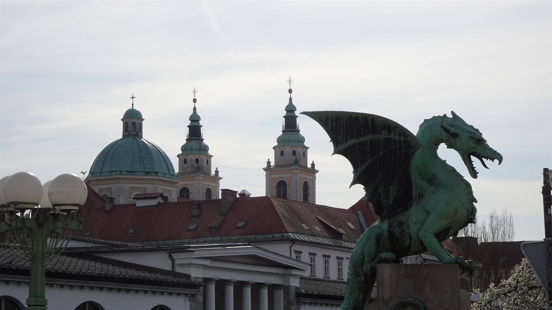 Statua di drago di rameverde sul ponte, cupola e campanili di Lubiana dietro