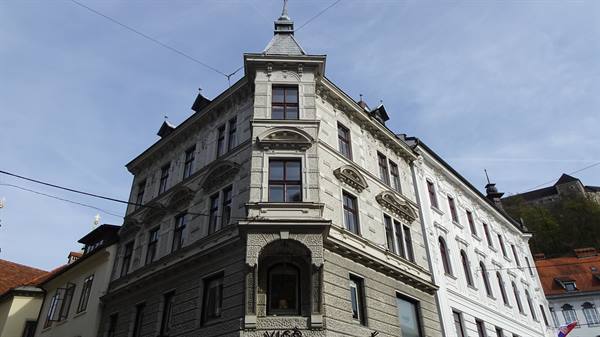 Ornate stone corner building in Ljubljana, castle visible on the hill