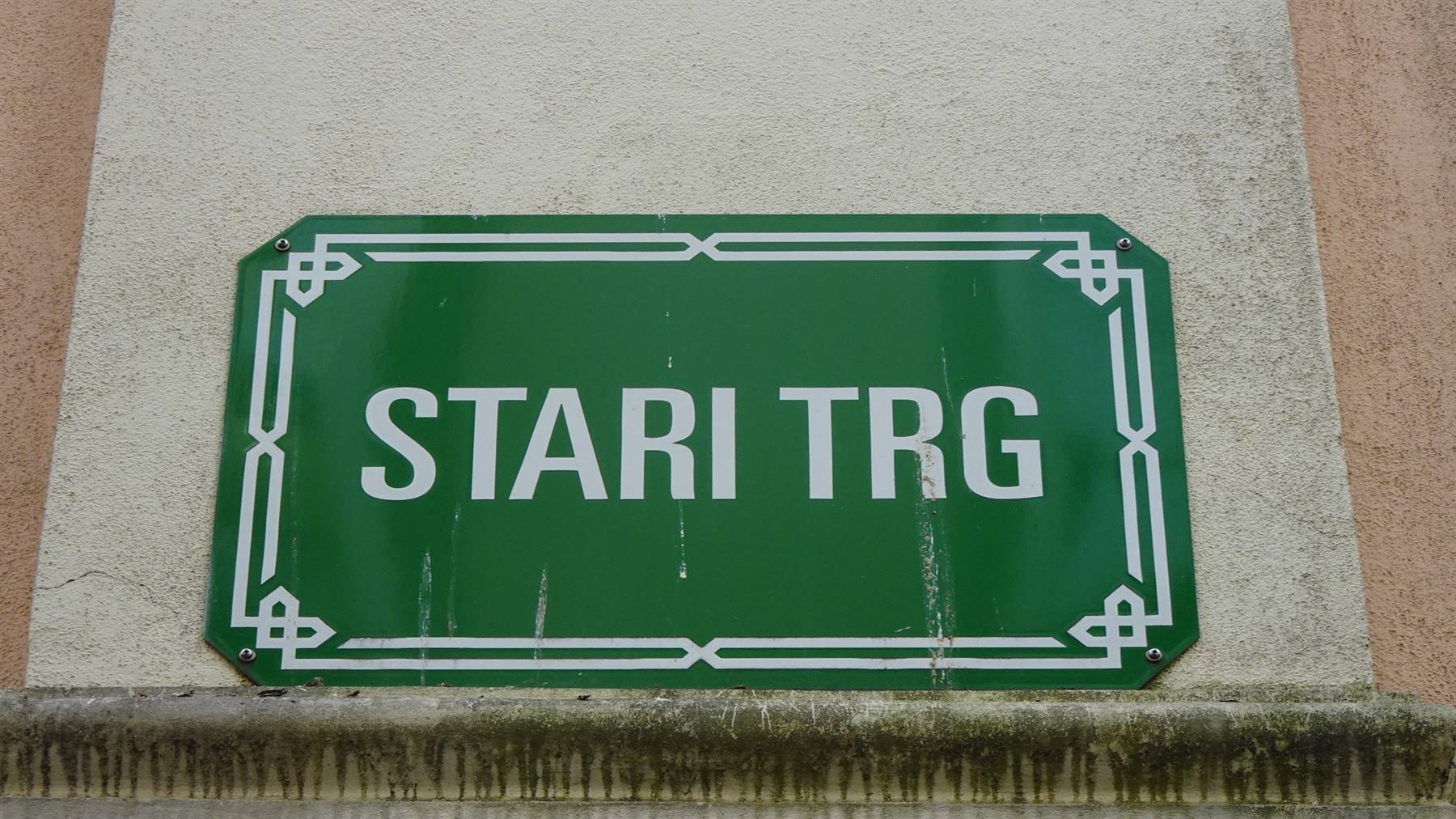 Cartello stradale verde con scritta bianca Stari Trg su muro intonacato