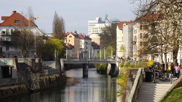 Stone bridge over the Ljubljanica river in Ljubljana, people walking on sunny banks