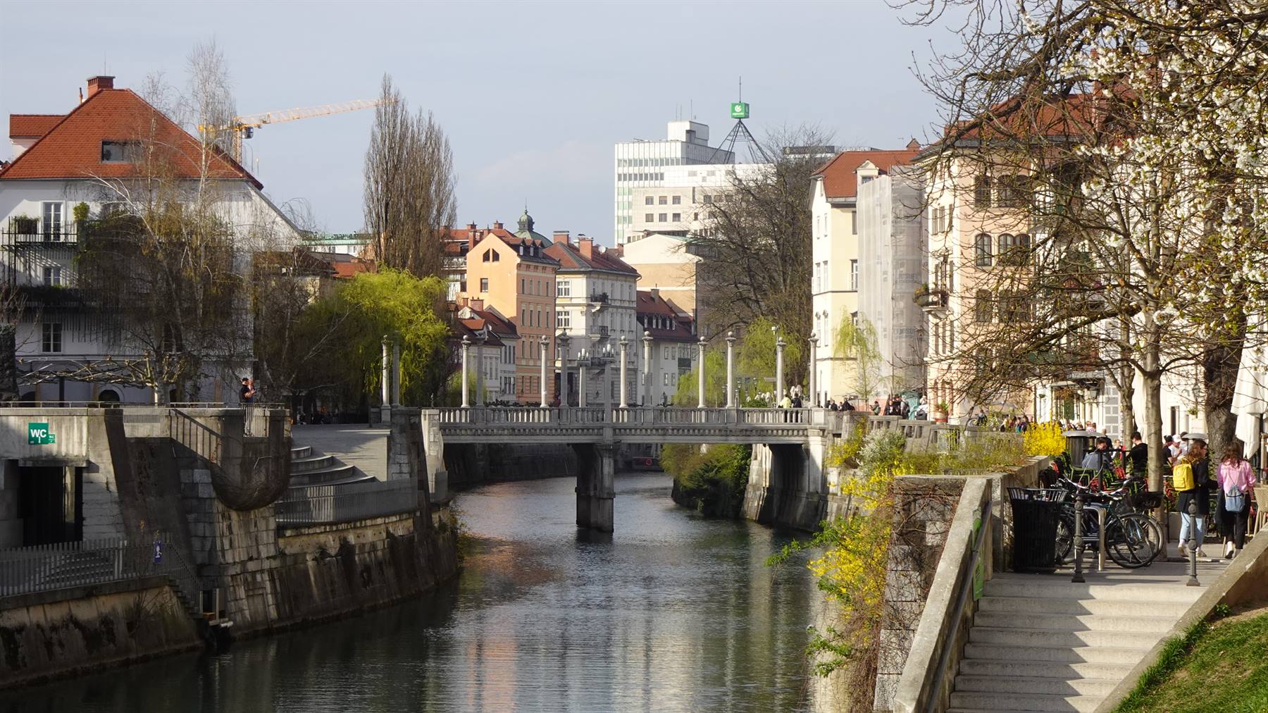 Ponte in pietra sul fiume a Lubiana, gente cammina lungo le rive insole