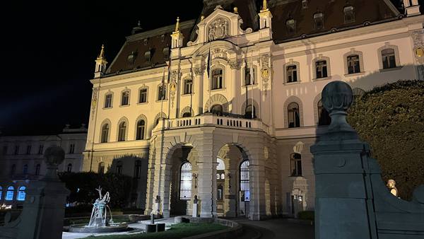 Illuminated palace at night with arched entrance and fountain in front