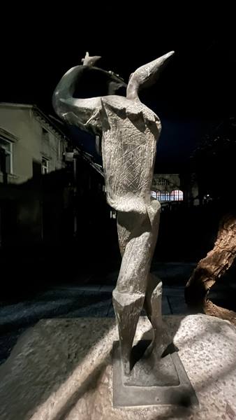 Stone sculpture of winged figure, lit at night on urban street