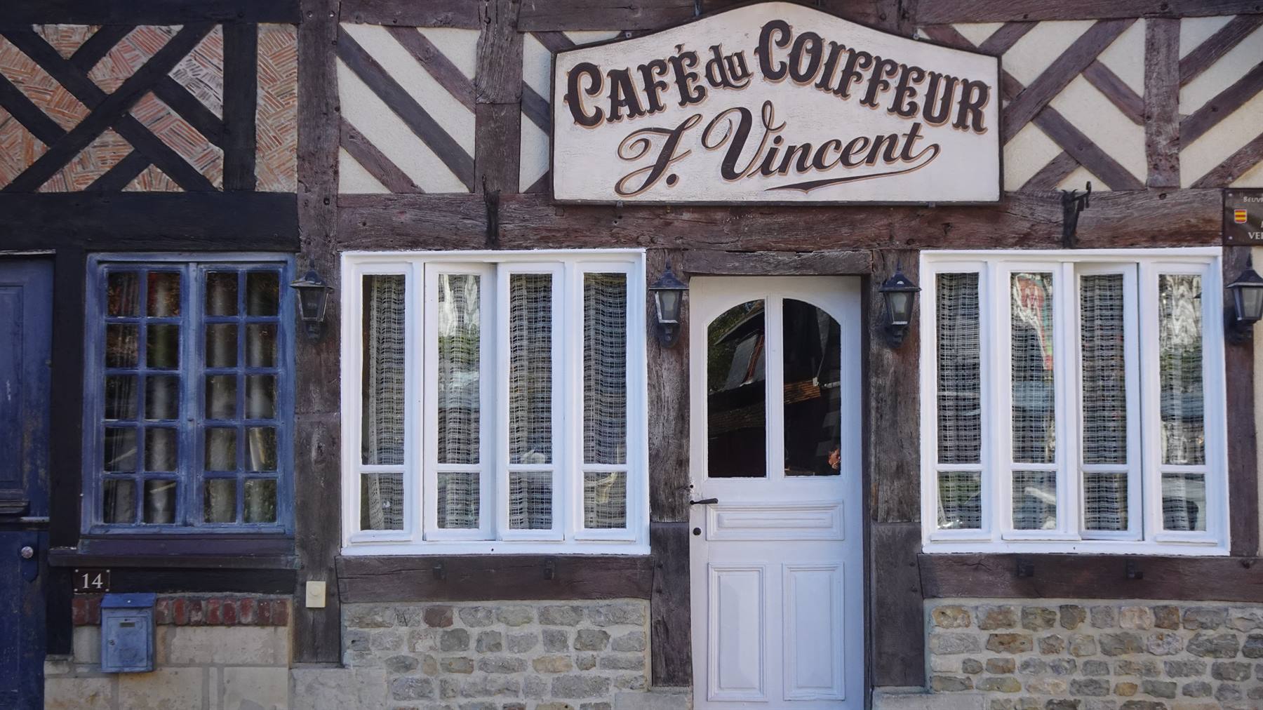 Insegna Cafè du Coiffeur F. Vincent su facciata a graticcio, porta bianca e finestre