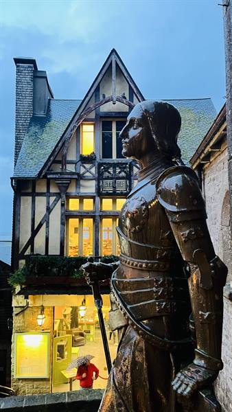 The statue watches over the old village as the rain lights up the lamps.