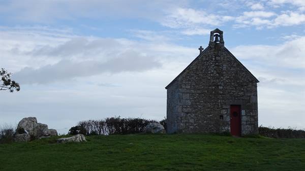 Stone chapel with bell tower and red door on grassy hill