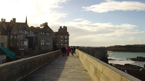 Tourists walk on the stone causeway toward the walled city of Saint-Malo
