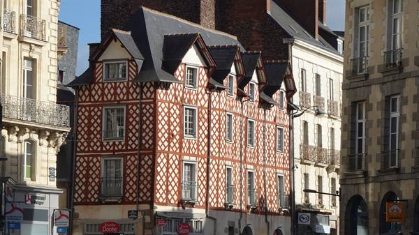 Half-timbered Renaissance house among stone buildings, sunlight, urban corner