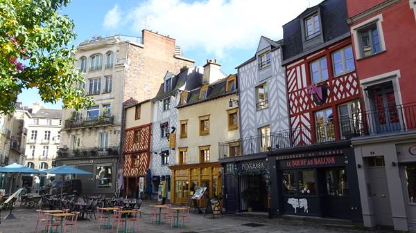 Colorful half-timbered houses line a square with café tables in Rennes