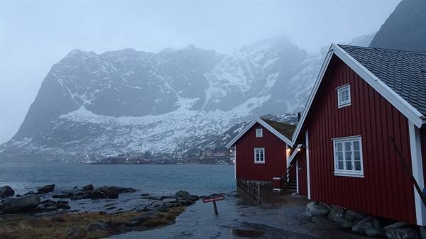 Red wooden cabin by the sea, snowy mountains in mist, Lofoten