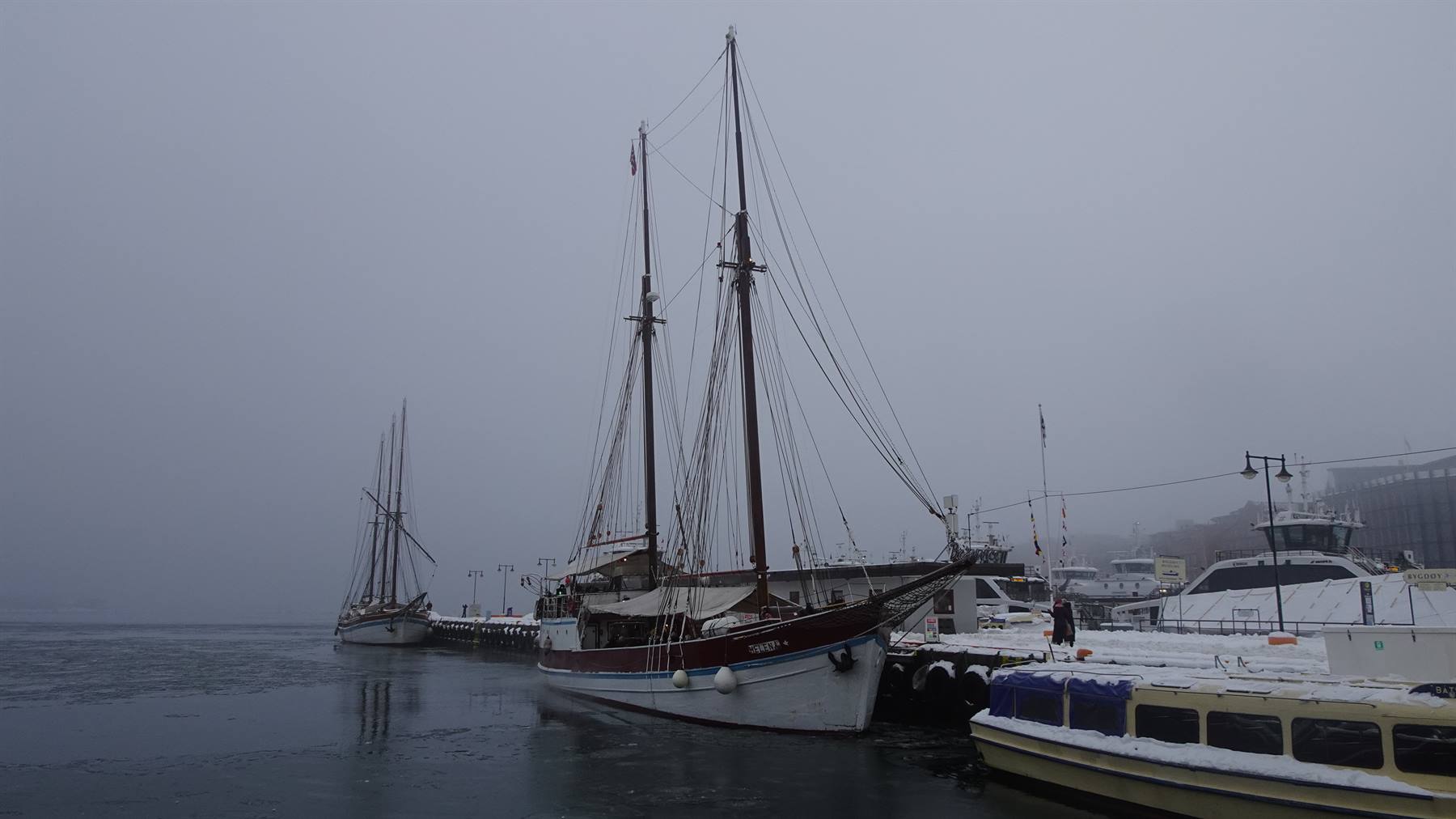 Veliero in legno ormeggiato al molo nella nebbia, neve sul ponte dei traghetti