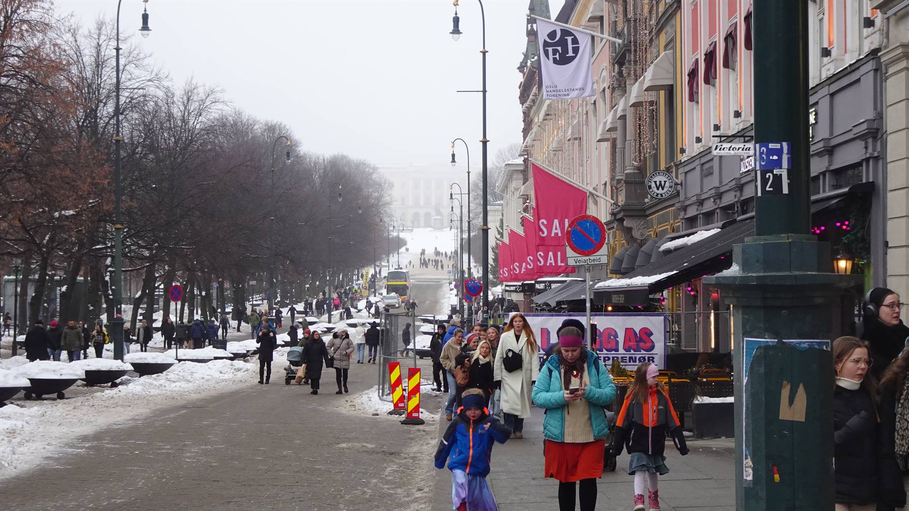 Pedoni lungo Karl Johans gate innevata, insegne e bandiere rosse, luce grigia invernale
