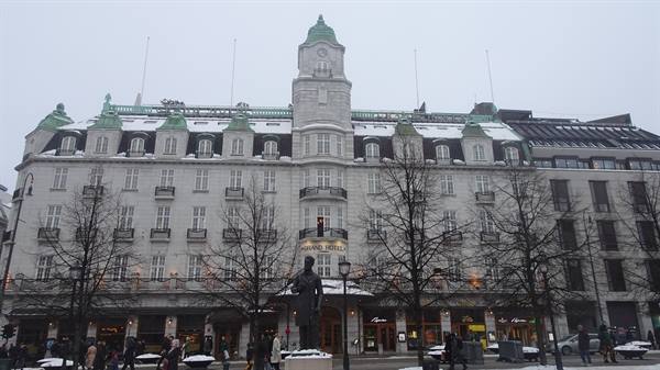 Statue in front of Oslo's snow-covered Grand Hotel under a grey sky